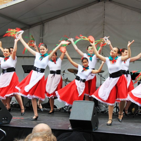 Young women in red and white dresses performing a dance at the Norton Street Festival